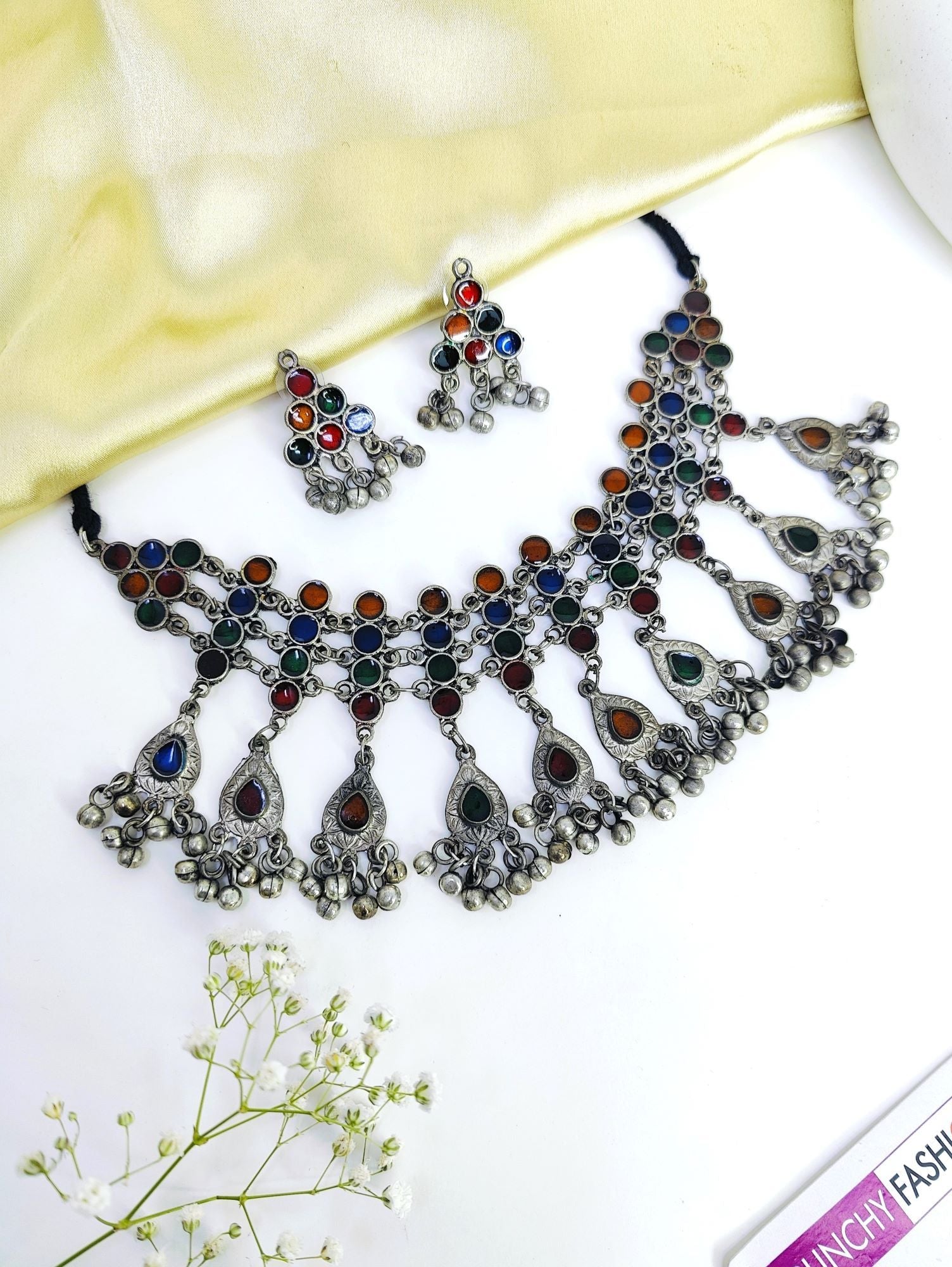 Oxidised jewellery set featuring an asymmetric choker necklace and pierced earrings. Crafted from alloy and gemstones, this silver Boho Fashion-inspired set is ideal for women and girls attending festivals, parties and weddings.