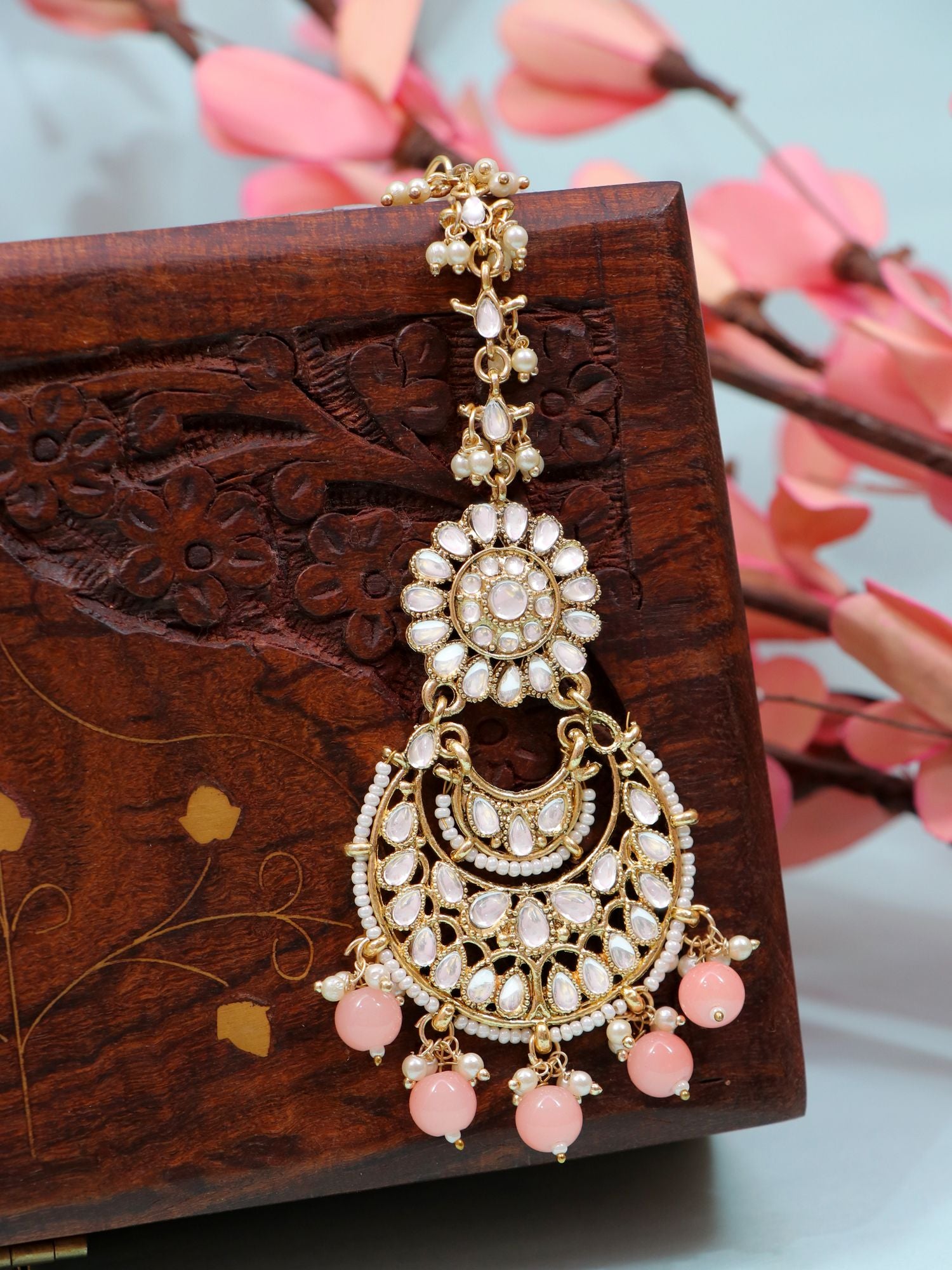 Ethnic maang tikka jewellery in gold and light pink colour, made of alloy, with an asymmetric design ideal for women and girls on festive, wedding, or anniversary occasions